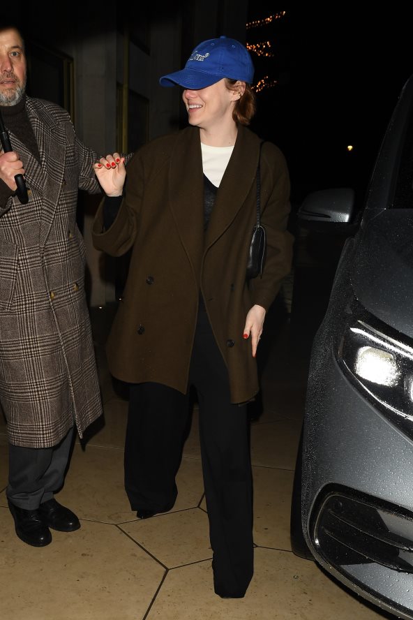 Glumica Emma Stone u braon kaputu, crnom džemperu i sa plavim kačketom.