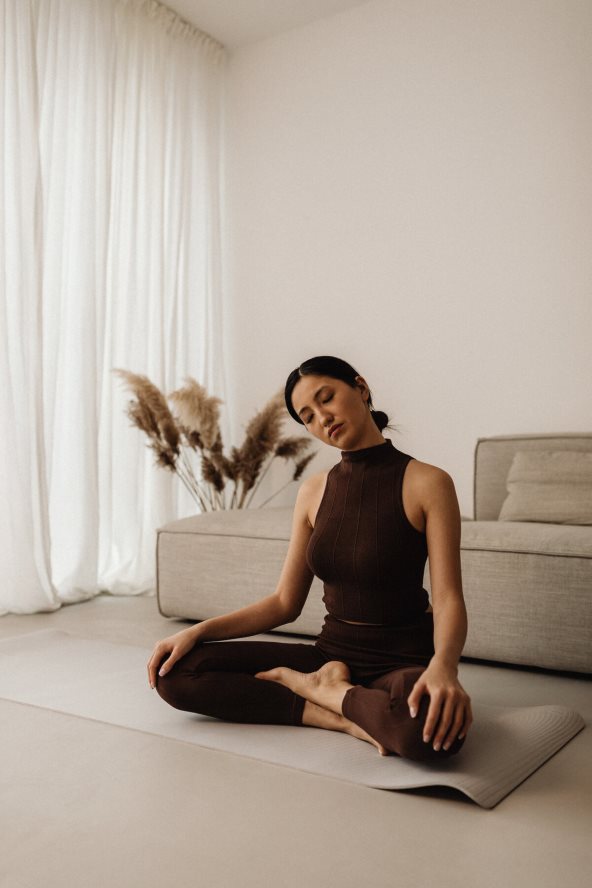 Žena vežba pilates na sivoj prostirci za trening.